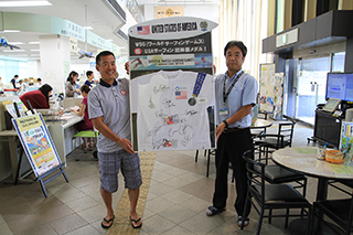 パネルを持ち笑顔のUSOC東京駐在員・ジョン大森氏（左）の画像