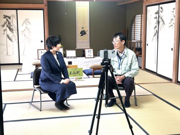 平田寺にて市担当者に王位戦でのエピソード等インタビューする加藤桃子氏